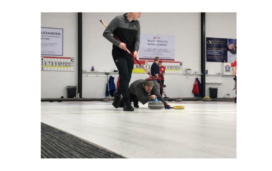 A curler at the Cincinnati Curling Club prepares to slide his stone down the ice while a teammate with a broom stands ready to sweep a clear path for it. 