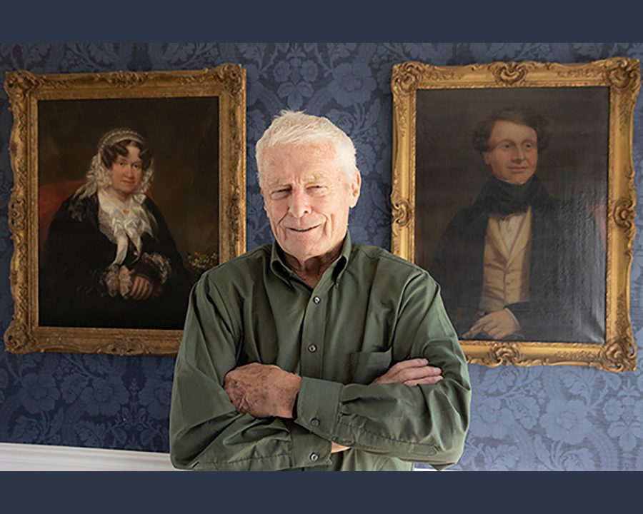 Richard Cocks stands in his Indian Hill home between the two first paintings he purchased. They are mid-19th century paintings of a man and a woman. 
