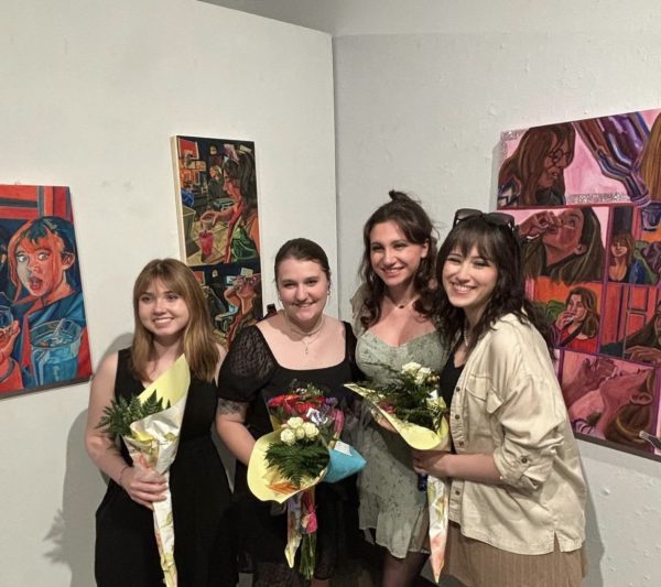 (From right to left) Melanie Schaefer and Gianna Velotta are posing with Velottas artwork during their Capstone exhibition.
