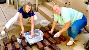 At the Red Brick Reunion Porsche Car Show, the prizes for the show are actual old bricks from the streets. Winners cherish the bricks and love displaying their Porsches in the uptown location. Kim Daggy (left) washed the bricks herself with some help. Photo provided by Kim Daggy
